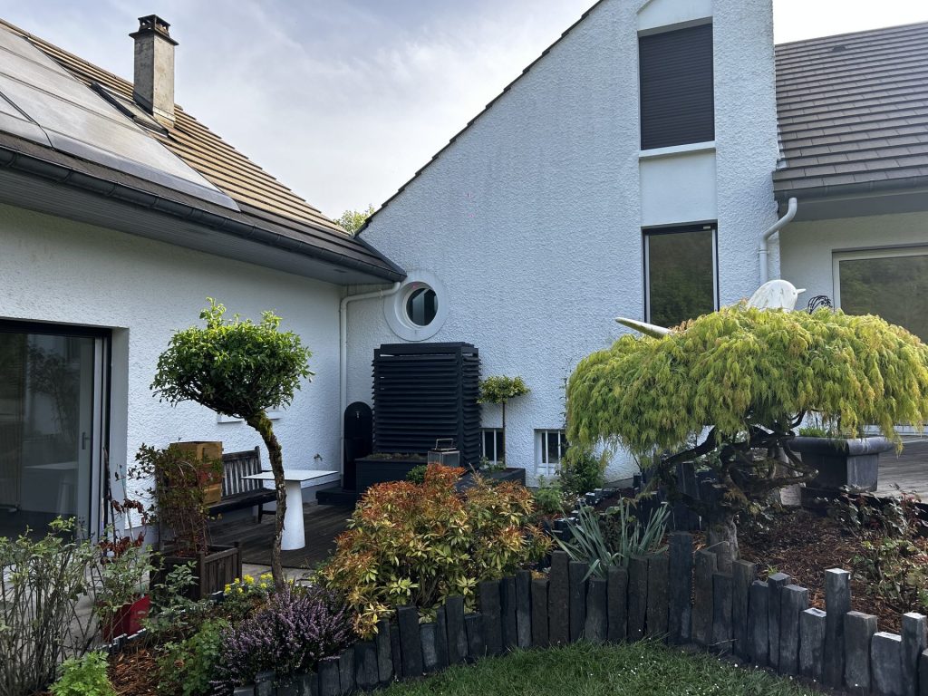 Jardin paysager avec cache climatisation intégré, arbre taillé, massif végétal structuré et bordures en pierre ardoise.