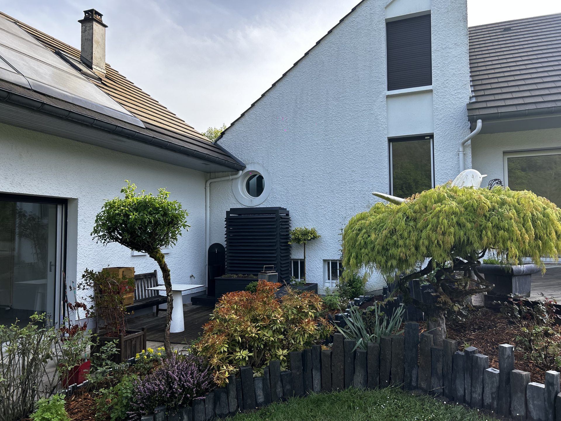 Jardin paysager avec cache climatisation intégré, arbre taillé, massif végétal structuré et bordures en pierre ardoise.